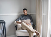 A man sitting on a chair in the corner of a room reading his WeNatal Manifestation Journal